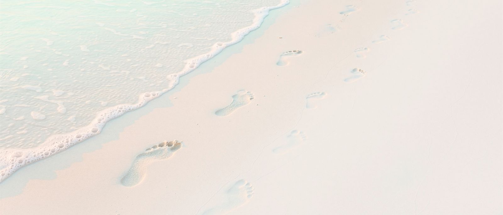 Footprints of an adult and a small child in white sand at the water's edge
