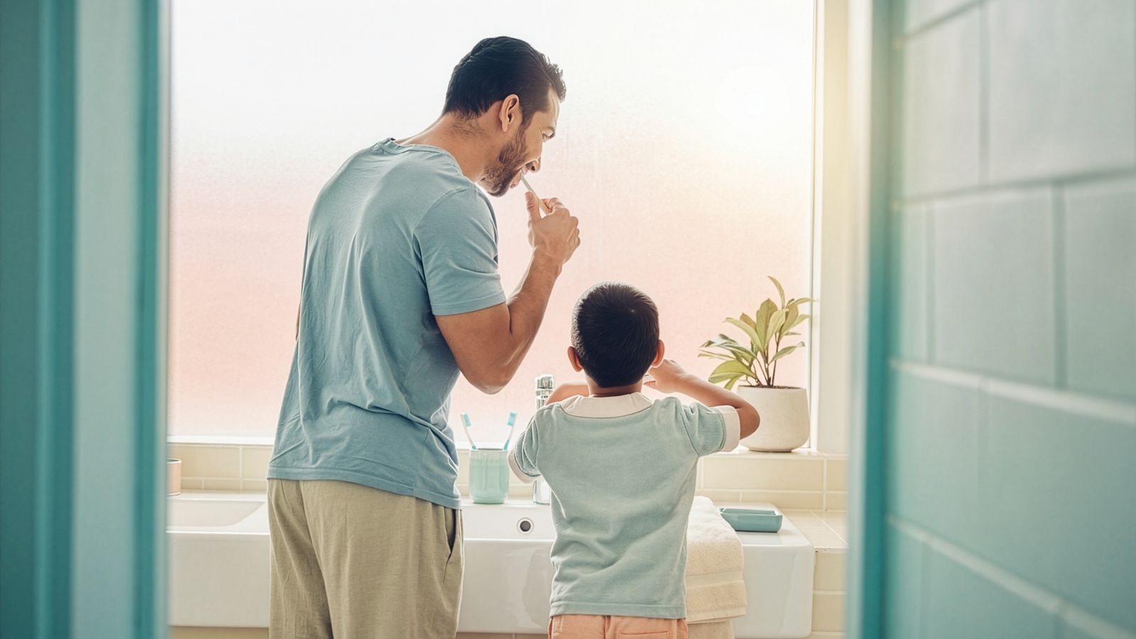 An adult and a young child brushing their teeth together at a bathroom sink